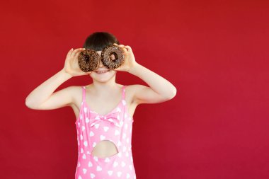 Stüdyoda elinde donutla ve lastik yüzükle poz veren mayolu sevimli küçük bir kız resmi. Havada yüzen güzel bir kız çocuğu.
