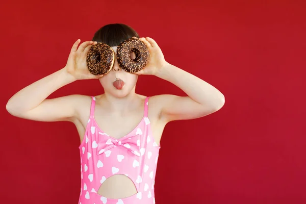 Tiro isolado de menina encantadora em maiô posando em estúdio com anel de borracha e segurando donut em sua mão. Menina bonita segurando círculo inflável de natação — Fotografia de Stock