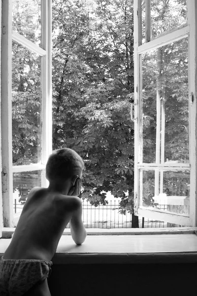 O rapaz está a olhar pela janela — Fotografia de Stock