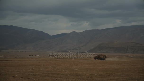 Φορτωμένο φορτηγό οδήγησης σε ένα χώρο με λόφους και τα βουνά στο φόντο στη διάρκεια της ημέρας με συννεφιασμένο ουρανό — Αρχείο Βίντεο