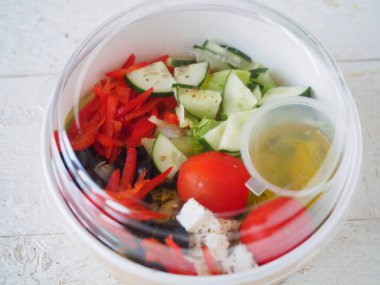 Beyaz ahşap masa üzerinde Yunan salatası ile karton konteyner