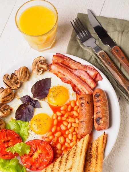 Colazione all'inglese completa con salsicce, pomodori e funghi alla griglia, uova, pancetta, fagioli al forno, pane con succo d'arancia — Foto Stock