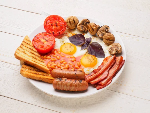 Desayuno inglés completo con salchichas, tomates y champiñones a la parrilla, huevo, tocino, frijoles horneados, pan con jugo de naranja —  Fotos de Stock