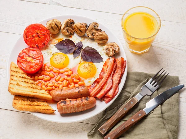 Café da manhã inglês completo, incluindo salsichas, tomates grelhados e cogumelos, ovo, bacon, feijão assado, pão com suco de laranja — Fotografia de Stock