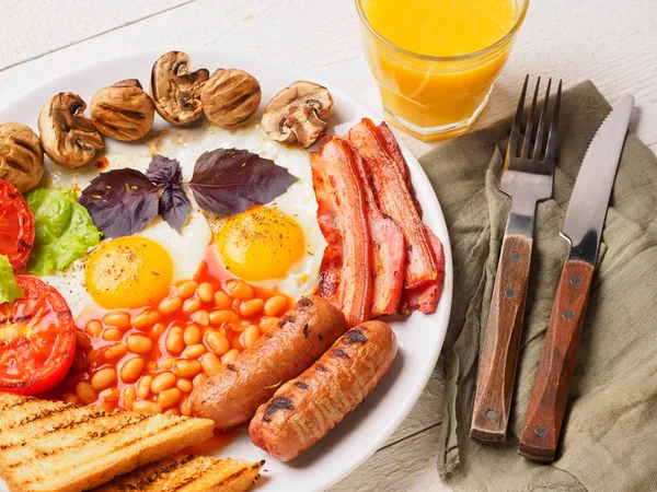 全英式早餐包括香肠、 烤的番茄和蘑菇、 鸡蛋、 培根、 烤的豆子，面包用橙汁 — 图库照片