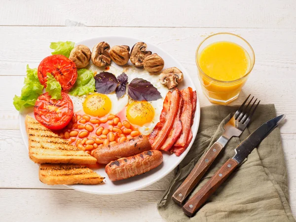 全英式早餐包括香肠、 烤的番茄和蘑菇、 鸡蛋、 培根、 烤的豆子，面包用橙汁 — 图库照片