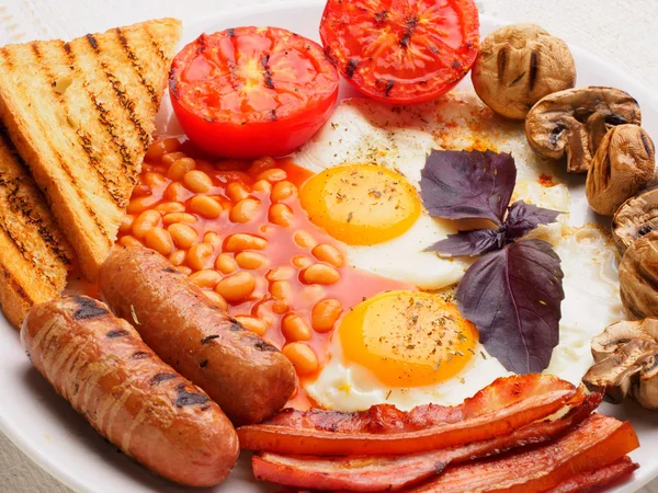 Desayuno inglés completo con salchichas, tomates y champiñones a la parrilla, huevo, tocino, frijoles horneados, pan con jugo de naranja —  Fotos de Stock