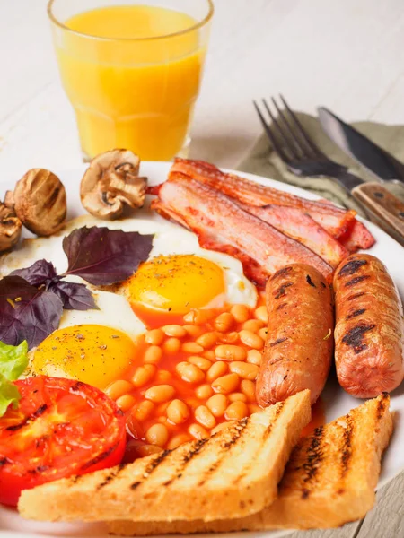 Desayuno inglés completo con salchichas, tomates y champiñones a la parrilla, huevo, tocino, frijoles horneados, pan con jugo de naranja — Foto de Stock