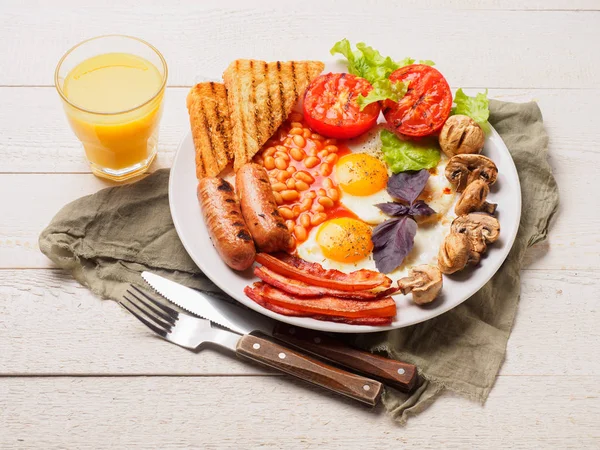 Desayuno inglés completo con salchichas, tomates y champiñones a la parrilla, huevo, tocino, frijoles horneados, pan con jugo de naranja —  Fotos de Stock