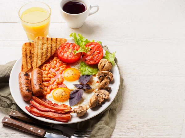 Desayuno inglés completo con salchichas, tomates y champiñones a la parrilla, huevo, tocino, frijoles horneados, pan con jugo de naranja — Foto de Stock