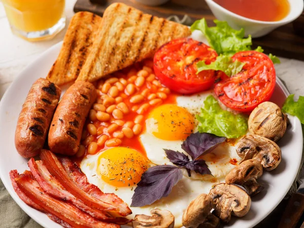 Kompletní anglická snídaně včetně klobásy, Grilovaná rajčata a houby, vejce, slanina, pečené fazole, chléb s pomerančovým džusem — Stock fotografie