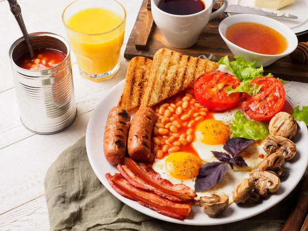 Desayuno inglés completo con salchichas, tomates y champiñones a la parrilla, huevo, tocino, frijoles horneados, pan con jugo de naranja —  Fotos de Stock