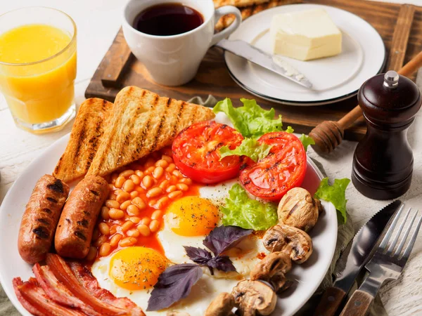 Englisches Frühstück mit Würstchen, gegrillten Tomaten und Pilzen, Ei, Speck, gebackenen Bohnen, Brot mit Orangensaft — Stockfoto