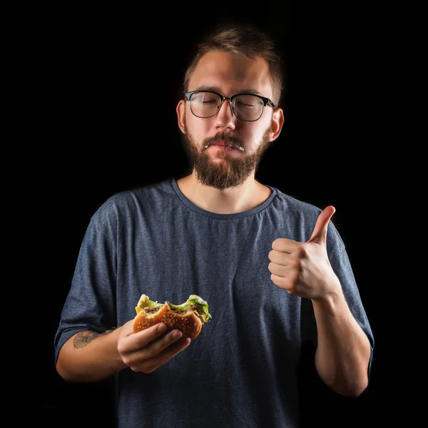 Joven comiendo una hamburguesa de comida rápida aislada en negro — Foto de Stock