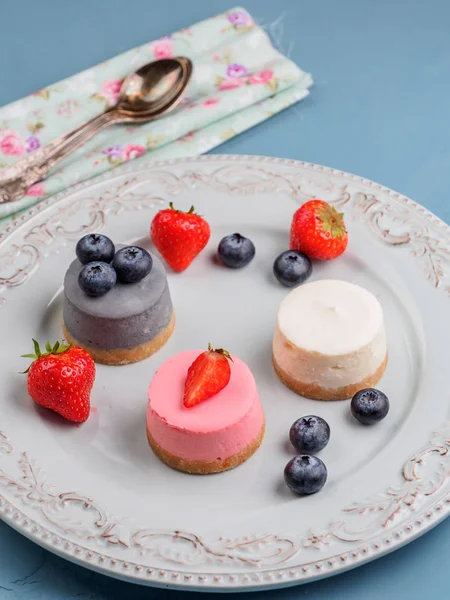 Маленькие круглые ягодные чизкейки на блюдечке и синем фоне — стоковое фото