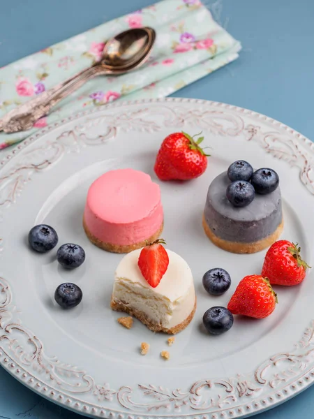 Küçük berry cheesecakes plaka ve mavi arka plan üzerinde yuvarlak — Stok fotoğraf