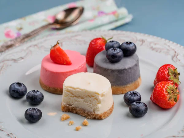 Kleine runde Beerenkäsekuchen auf Teller und blauem Hintergrund — Stockfoto