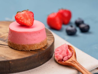 Küçük yuvarlak ahşap masa ve mavi arka plan üzerinde çilek cheesecakes