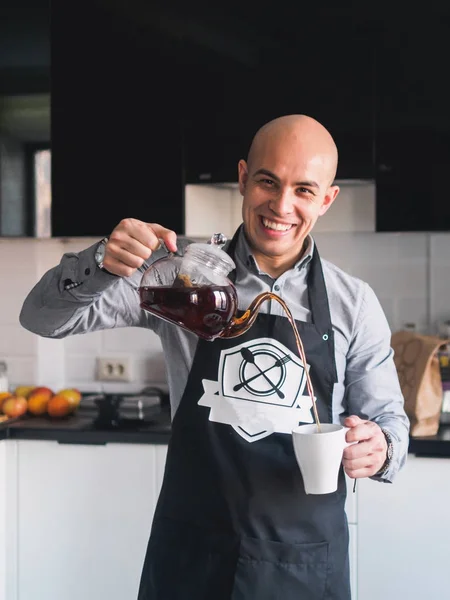 Calvo feliz hombre en delantal con tetera en la cocina — Foto de Stock