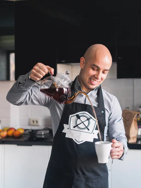 Calvo feliz hombre en delantal con tetera en la cocina — Foto de Stock