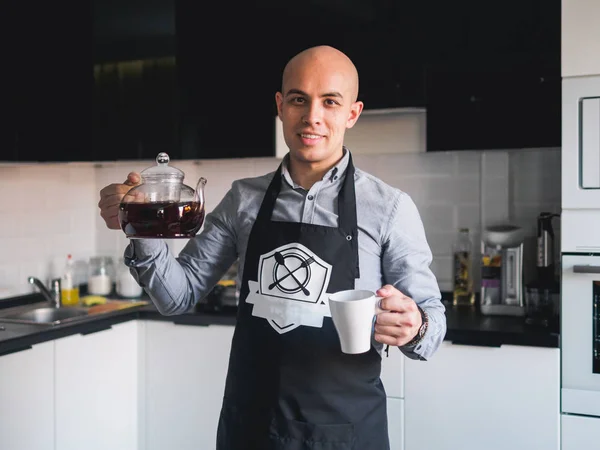 Calvo feliz hombre en delantal con tetera en la cocina — Foto de Stock