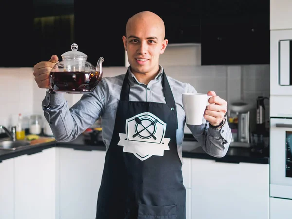 Calvo feliz hombre en delantal con tetera en la cocina — Foto de Stock