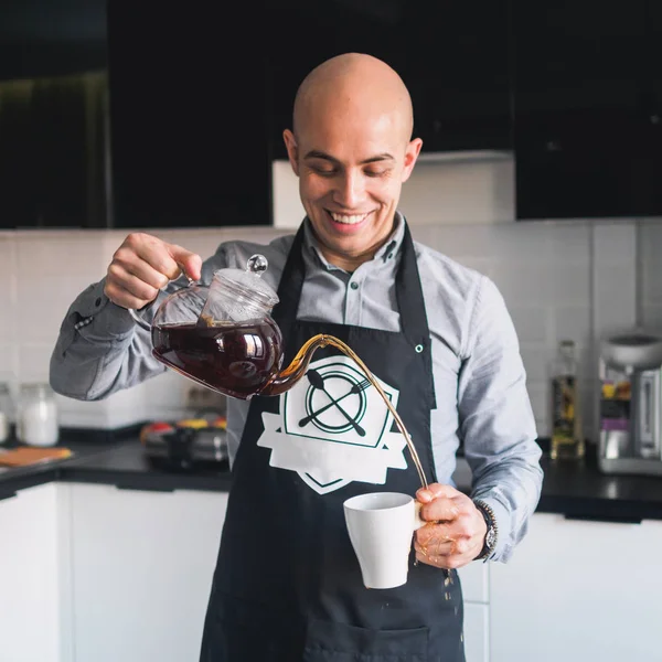 Calvo feliz hombre en delantal con tetera en la cocina — Foto de Stock