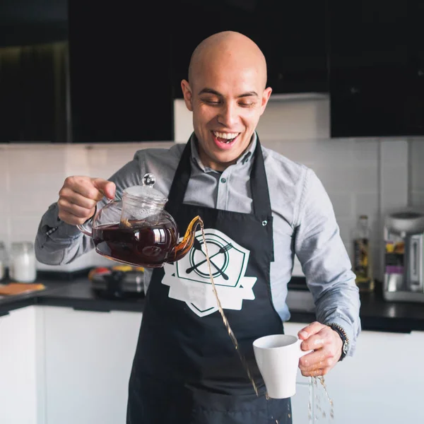 Calvo feliz hombre en delantal con tetera en la cocina — Foto de Stock