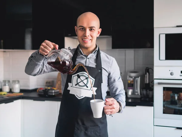 Лысый счастливый человек на фартуке с чайником на кухне — стоковое фото