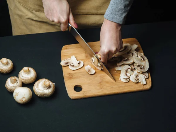 Vrouw snijden rauwe paddestoelen op een houten bord — Stockfoto