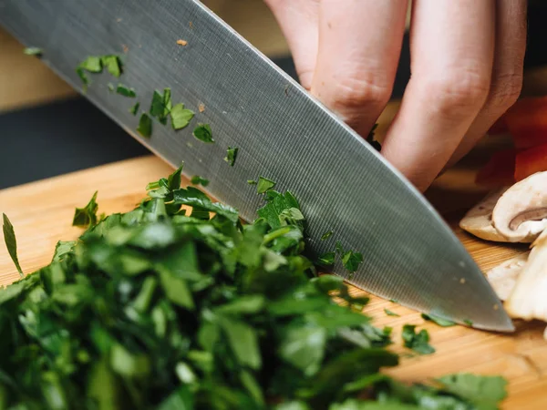 Vrouw snijden peterselie Groenen op houten bord — Stockfoto
