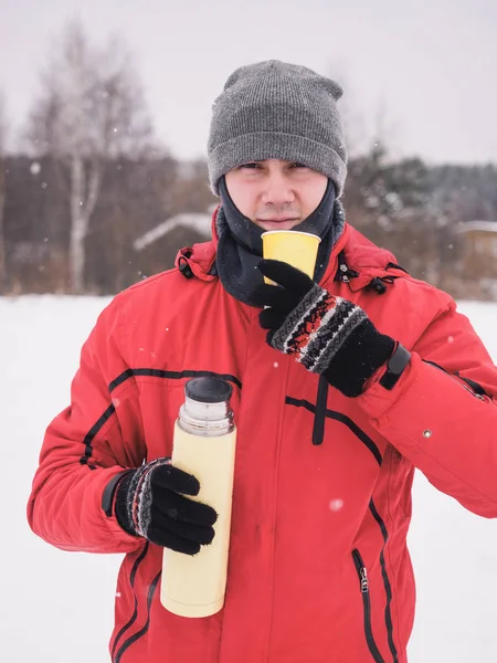Посміхайтеся зимою заморожений молодий чоловік з термосом і чашкою — стокове фото