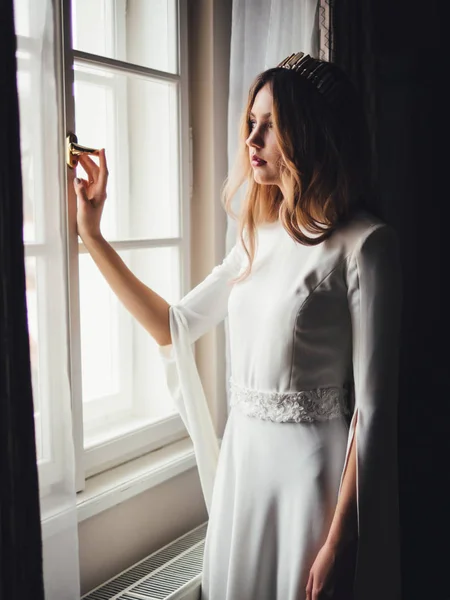 Mariée près de la fenêtre. robe de mariée européenne blanche avec diadème de tiare — Photo