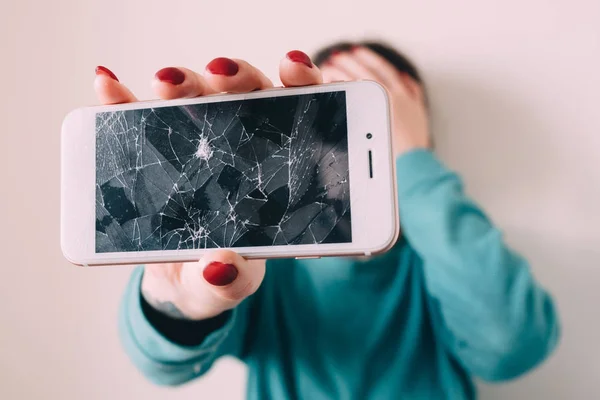 Broken glass screen smartphone in hand of upset girl, white background
