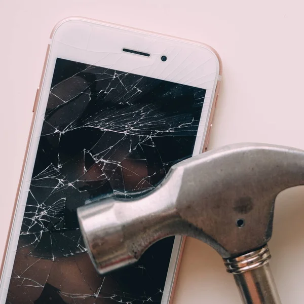 broken screen of smartphone with hammer on white table