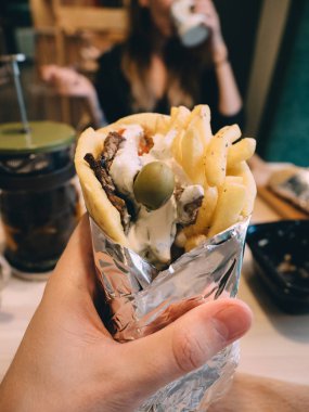 Ellerinde sos, sebze, peynir ve patates kızartması olan Yunan etli jiroskopları.