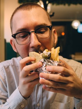 Ellerinde sos, sebze, peynir ve patates kızartması olan Yunan etli jiroskopları.