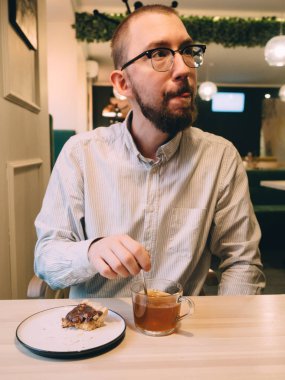 Kafede sakallı ve gözlüklü bir adam tatlı çayı içer.