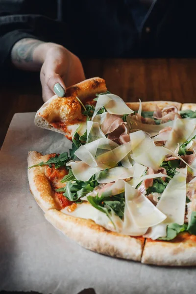 Pizza with parma ham, cheese, arugula, sauce in rustic cafe table