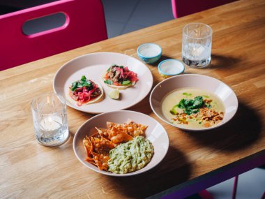 Nachos, guacamole, taco, çorba ve mumlar bar masasında.