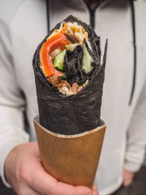 Shawarma 'lı donör siyah pidanın içinde insan ellerinde yuvarlanıyor.