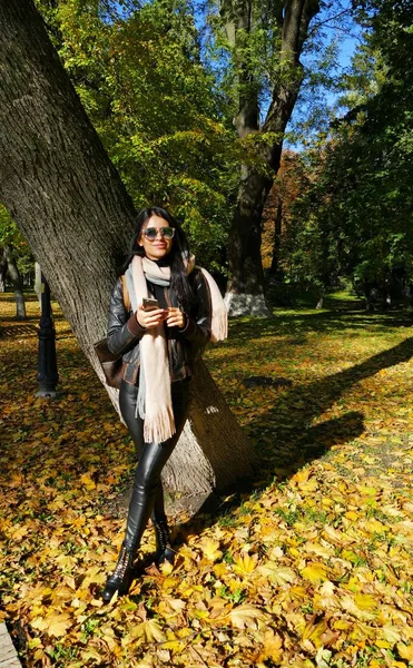  büyük bir ağaç bir sonbahar Park yakınındaki poz deri pantolonlu güzel kız