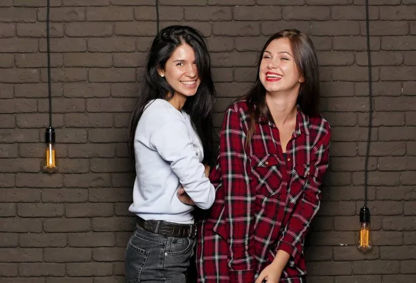 İki genç ve güzel kadının tuğla duvara yakın poz olan