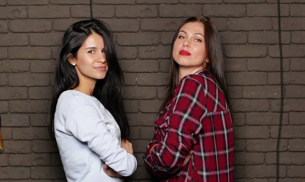 İki genç ve güzel kadının tuğla duvara yakın poz olan