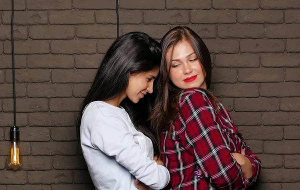 İki genç ve güzel kadının tuğla duvara yakın poz olan