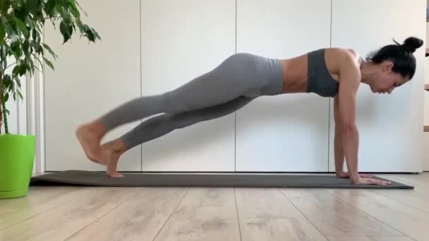 スポーツウェアの若いフィットネス女性は自宅やスタジオでプランク運動を行う 隔離中の動的板 胃の筋肉を動作させる演習 — ストック動画