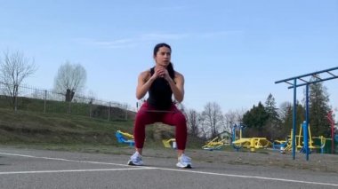 Kadın spor antrenmanı ve sabah dışarıda çalışma. Güçlü ve sportif kadın hamleler yapıyor, çömeliyor, burpee yapıyor.