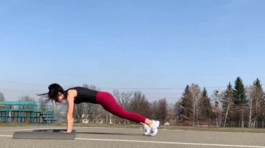 Kadın spor antrenmanı ve sabah dışarıda çalışma. Güçlü ve sportif kadın hamleler yapıyor, çömeliyor, burpee yapıyor.