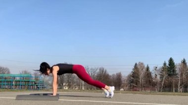Kadın spor antrenmanı ve sabah dışarıda çalışma. Güçlü ve sportif kadın hamleler yapıyor, çömeliyor, burpee yapıyor.
