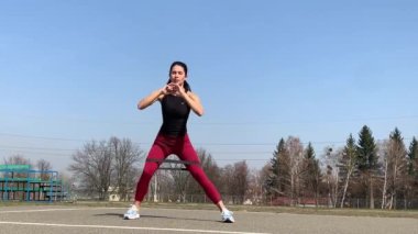 Kadın spor antrenmanı ve sabah dışarıda çalışma. Güçlü ve sportif kadın hamleler yapıyor, çömeliyor, burpee yapıyor.